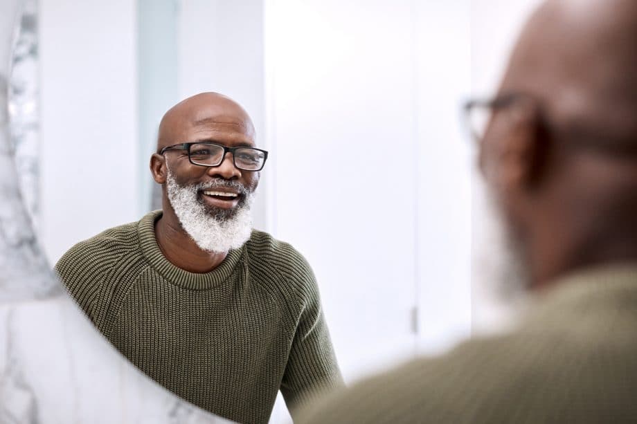 man with white beard looking at his smile in the mirror