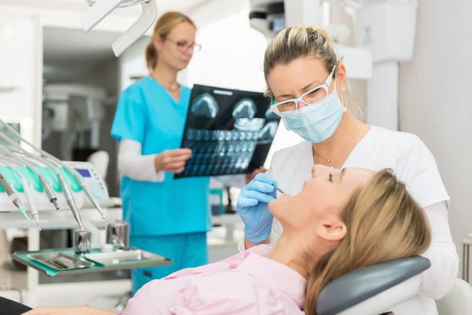 dentist looking at xray chart while assistant looking in patients mouth