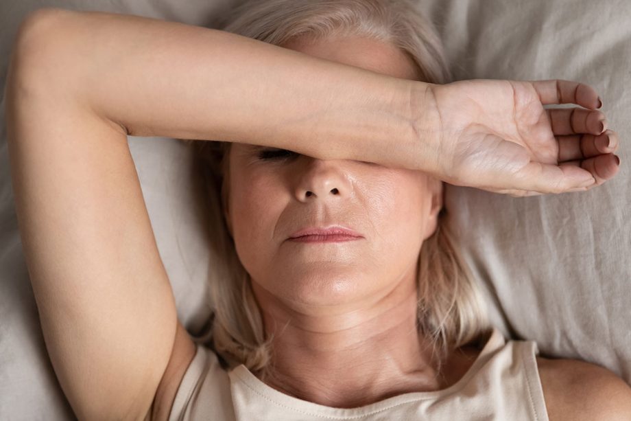 middle aged woman laying in bed with arm over face